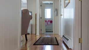 Un pasillo con suelo de madera, una zona alfombrada y una puerta a la derecha.