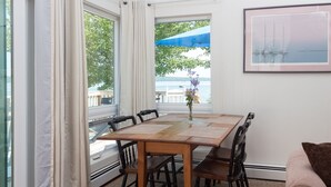 Un comedor con una mesa y sillas de madera, un florero con flores y vista al lago a través de amplios ventanales.