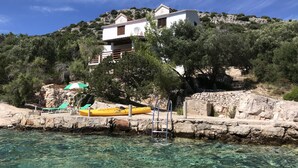 Una casa costera con vista despejada al mar, un kayak amarillo y un paraguas verde.