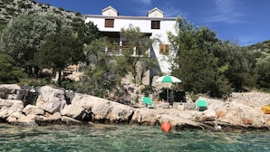 Un edificio costero con fachada blanca, escalones de piedra que conducen a él y una vista despejada del mar.