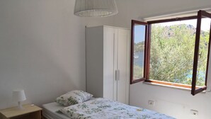 Un dormitorio pequeño con cama, mesita de noche, armario y ventana con vistas a zonas verdes y un cuerpo de agua.