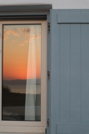 Ein Fenster mit Blick auf einen Sonnenuntergang über dem Wasser.