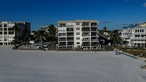 A beachfront hotel with multiple balconies, a sandy beach in the foreground, and palm trees in the background.
