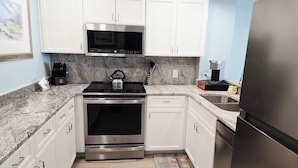 A kitchen with white cabinets, a stainless steel refrigerator, a microwave, a stove, and a coffee maker.