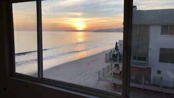 A view of a beach from a window overlooking a building with a balcony.