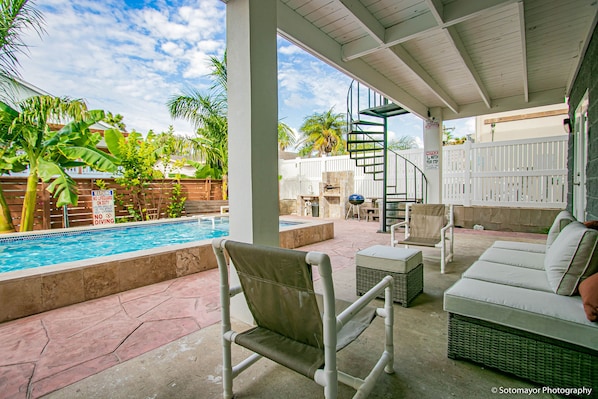 A covered outdoor area with a pool, seating, and a spiral staircase.