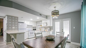 Une cuisine moderne avec des meubles blancs, une table à manger en bois et un luminaire suspendu.