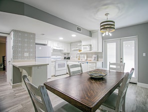A modern kitchen with white cabinets, a wooden dining table, and a hanging light fixture.