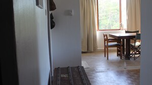 A hallway with a wooden chest, a dining table with chairs, and a window with curtains. - Homely & Friendly property (DSM)