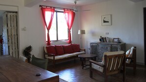 A living room with a wooden dining table, a sofa with red cushions, a wooden cabinet, and a ceiling fan. - Homely & Friendly property (DSM)