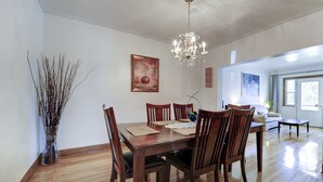A dining room with a wooden table and chairs, a chandelier, and a vase with branches.