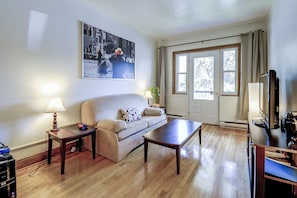 A living room with a sofa, a coffee table, a lamp, a TV, and a large window with curtains.