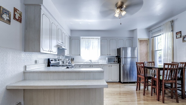 A modern kitchen with white cabinetry, a central island, stainless steel appliances, and a dining area with wooden chairs.
