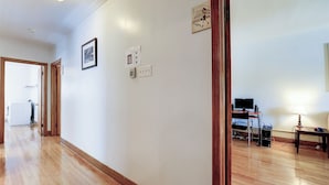 A hallway with wooden flooring, a door leading to a laundry area, and a desk with a computer and lamp.