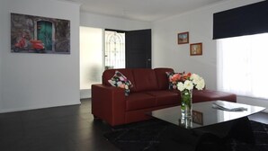 A modern living room with a red sofa, a glass coffee table, and a painting of a scooter on the wall.