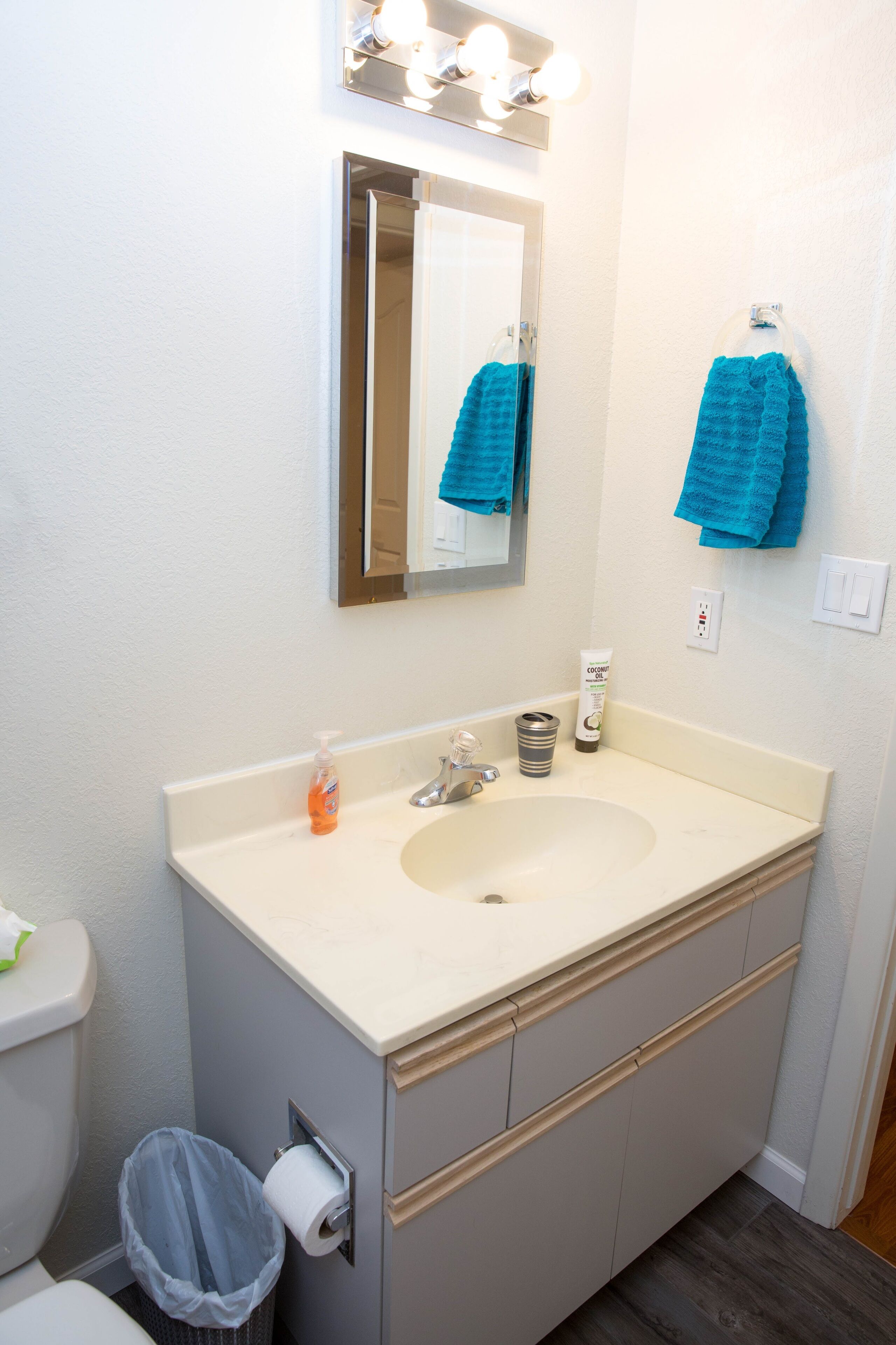 Un baño con lavamanos, espejo y dos toallas colgadas en la pared.