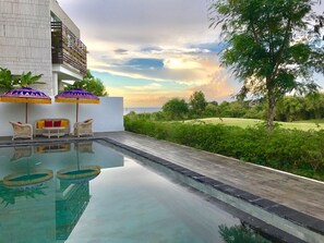 Un área de piscina con sillones de descanso y sombrillas, una terraza de madera y vistas al paisaje.