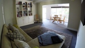 A living room with a sofa, a bookshelf, a dining area with chairs, and a large window.