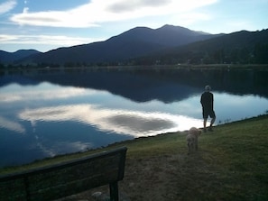 A person and a dog by a calm lake with mountains in the background. - Ride hard, Rest Easy, Sleep Well (Mount Beauty)