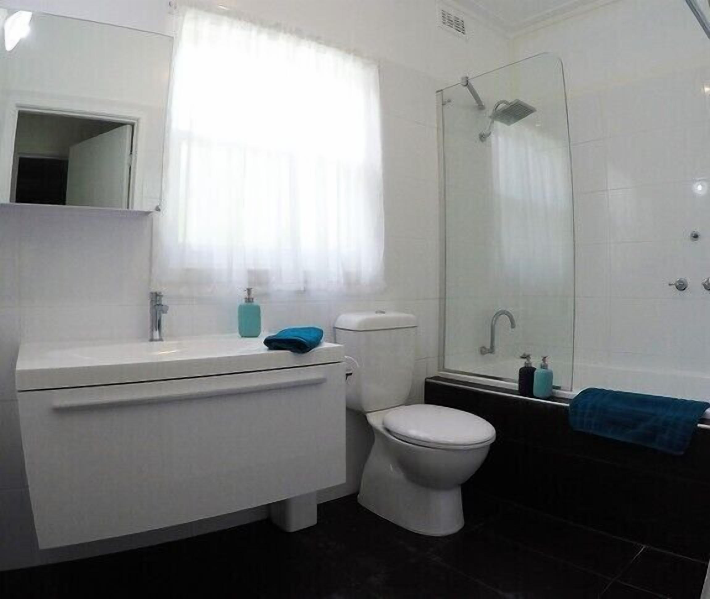 Un baño con lavamanos blanco, inodoro y ducha con mampara de vidrio.