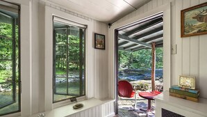 Ein Zimmer mit großen Fenstern, einem roten Sessel, einem Kamin und einem Bücherregal.