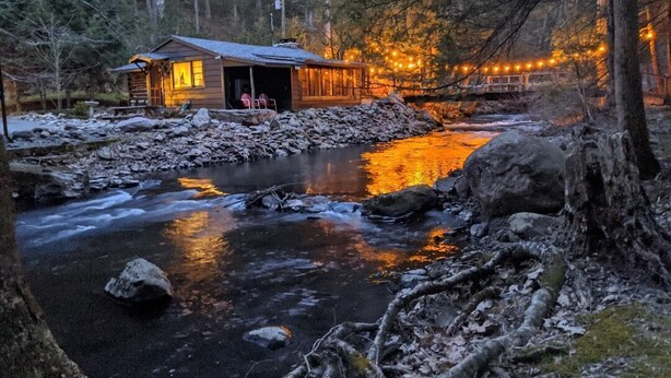 Ein rustikales Holzhäuschen an einem Fluss mit einer Holzfassade und einer kleinen Veranda.