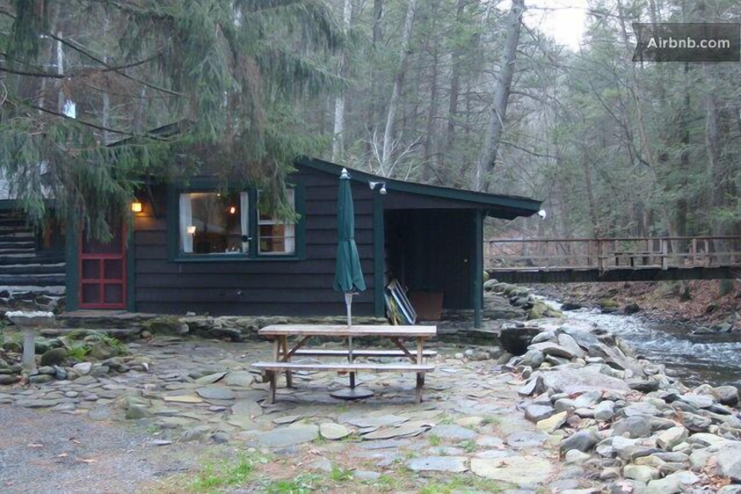 A rustic cabin with a red door, a wooden bench, and a picnic table in front.