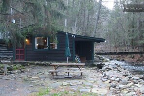A rustic cabin with a red door, a wooden bench, and a picnic table in front. - Get cozy at Big Al's Poconos Creek House - Wireless DSL and Trout!! (Stroudsburg)