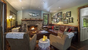 Ein gemütliches Wohnzimmer mit Kamin aus Stein, bequemen Sitzmöglichkeiten und gerahmten Kunstwerken an den Wänden.