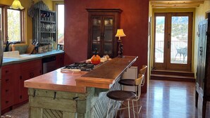 A kitchen with a central island, bar stools, a wooden cabinet, and a view through the door.