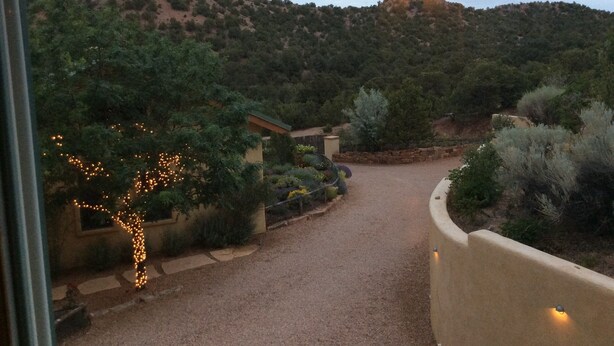 A gravel driveway leading to a building surrounded by landscaped gardens and a hilly backdrop.