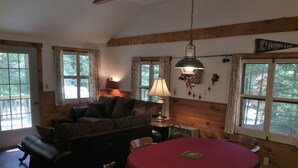 A cozy living room with a wooden ceiling, a couch, a table with a red tablecloth, and a lamp. - Beautiful lakeview cottage on Friends Lake (Chestertown)