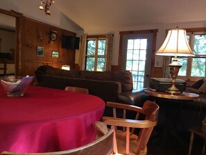 A cozy living room with a red table, wooden chairs, a sofa, and a lamp.