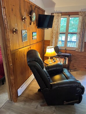 A room with a wooden wall, a black leather chair, a television, a lamp, and a bookshelf. - Beautiful lakeview cottage on Friends Lake (Chestertown)