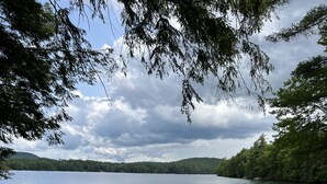 A lakeside view with a sandy beach, a dock with a boat, and a picnic table. - Beautiful lakeview cottage on Friends Lake (Chestertown)