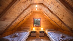 A cozy attic bedroom with two beds, wooden walls, a window, and a hanging light fixture. - Kuća za odmor "Neralić" (Modruš)
