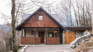 A wooden cabin with a stone wall and a wooden door, surrounded by trees and a gravel path. - Kuća za odmor "Neralić" (Modruš)