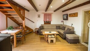 A living room with a wooden staircase, a sofa, a coffee table, and a dining table with chairs. - Kuća za odmor "Neralić" (Modruš)