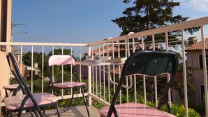 A balcony with two pink chairs and a table, white railing, and a view of a tree and buildings in the background. - Apartment Laura, Viškovići, Koromačno, Istra ! near the sea!!   (Koromačno)
