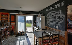 Eine gemütliche Küche mit einer Tafelwand, die verschiedene Fleischsorten auflistet, einem Holztisch mit Stühlen und Blick ins Freie.