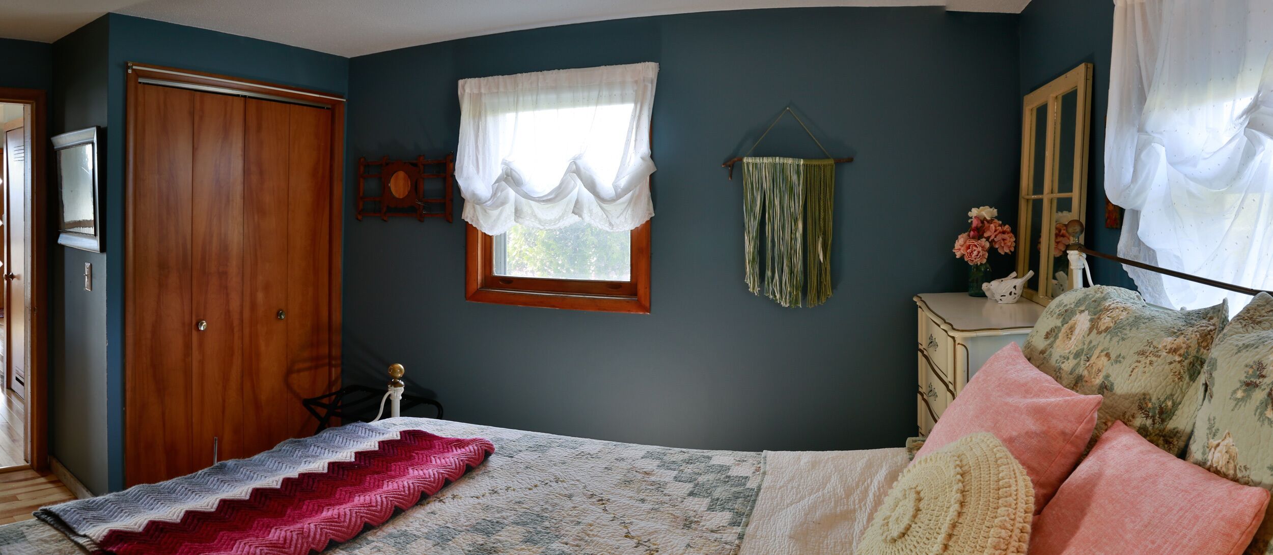 A bedroom with a bed, a dresser, a mirror, a window with curtains, and a door.