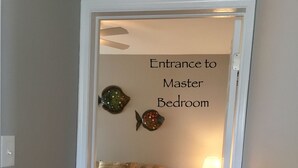 An entrance to a master bedroom with a bed, nightstand, lamp, and decorative fish wall art.
