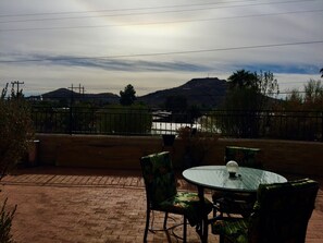 Eine Terrasse im Freien mit einem runden Glastisch und Stühlen, einem Backsteinboden und Blick auf einen See und Berge im Hintergrund.