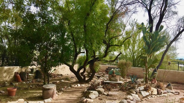Un jardín con una estatua de Buda, rocas y cactus.