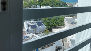 Vista a través de persianas de un edificio con jardín en la azotea y paneles solares, bajo un cielo azul despejado.