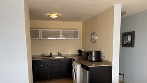 Una cocina compacta con armarios oscuros, microondas, cafetera y lavavajillas.