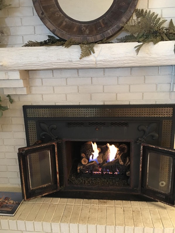 Una chimenea con revestimiento de ladrillo blanco, un espejo decorativo arriba y un repisa con plantas.