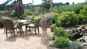 An outdoor patio with wicker furniture and a table, surrounded by potted plants and a stone wall.