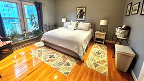 A bedroom with a large bed, two bedside tables with lamps, a window with curtains, and a framed picture on the wall. - Huge Space for 10 +pets Gated 6 cars;15 min walk- B’way; Pickle-ball ct 2bathrms (Nashville)