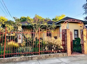 A residential house with a brick gate, a number '53' on the door, and a fenced yard with various plants.